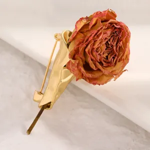 Makroansicht einer kreativen goldenen Blumenstrauß-Brosche mit einer echten Trockenrose
