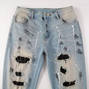 Close-up of distressed denim jeans with black rhinestone patches and paint splatters.