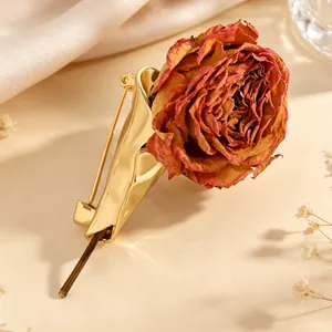 Detailed close-up of a unique gold-toned flower holder brooch featuring a dried rose