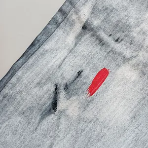 Primo piano di tessuto denim grigio consumato con un tratto di vernice rossa.