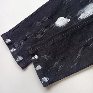 Dettaglio di jeans neri strappati con schizzi di vernice bianca e orlo sfilacciato