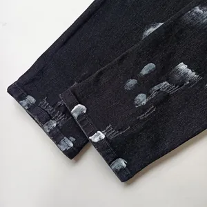 Dettaglio di jeans neri con design a schizzi di vernice grigia sugli orli.