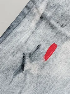Dettaglio di jeans neri da uomo con lavaggio grigio e tratto di vernice rossa vivace.