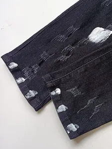 Jeans in denim nero slim fit con dettagli strappati e schizzi di vernice bianca sul fondo