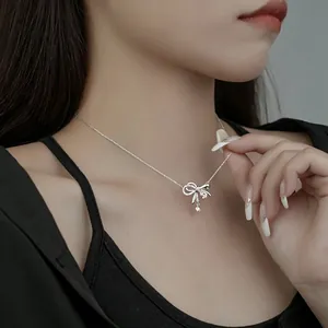 Close-up of a delicate silver bow necklace with pink zircon on model's neck