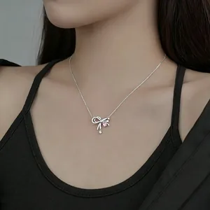 Detail view of a dainty silver bow necklace with pink and clear zircons worn by model