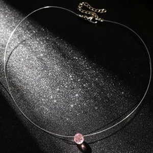 Detail van onzichtbare ketting met roze kristallen hanger op een schitterende zwarte achtergrond