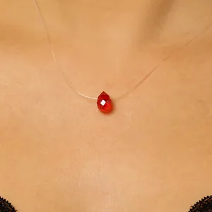Close-up van een onzichtbare visdraadketting met een rode kristallen druppelhanger.