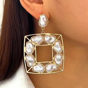 Dettaglio di un grande orecchino quadrato dorato con perle barocche irregolari.