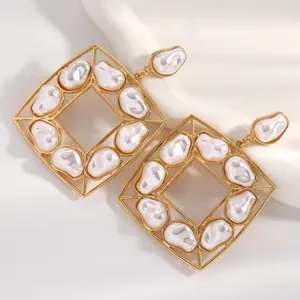 Primo piano di grandi orecchini geometrici dorati con perle barocche eleganti