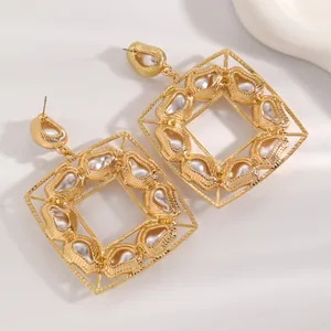 Primo piano di orecchini quadrati dorati con perle barocche e raffinato design cavo