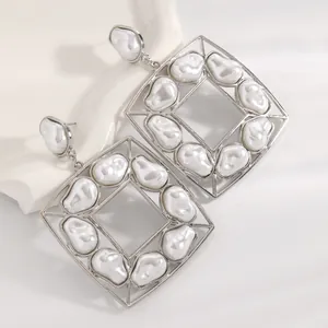 Dettaglio macro di grandi orecchini a perla barocca con montatura geometrica argento.