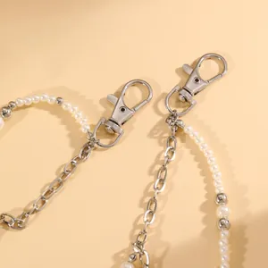 Dettaglio di una catena per pantaloni in perle finte e metallo argentato con mosquettoni.
