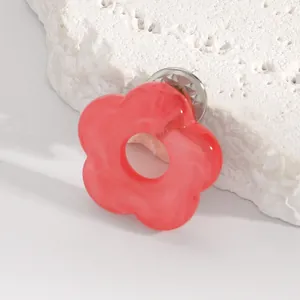 Close-up of a vibrant red hollow flower brooch with a marble texture on white stone.