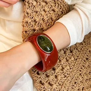 Stylish vintage wide acrylic bangle with an oval green accent stone on model's wrist