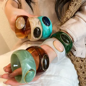 Detail view of retro wide acrylic bangles with oval stone inlays and gold rims