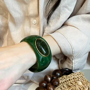 Retro wide green acrylic bangle with an oval dark inset worn on a wrist with linen shirt