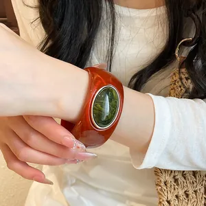 Macro shot of a vintage amber red acrylic wide bangle featuring an oval green resin center