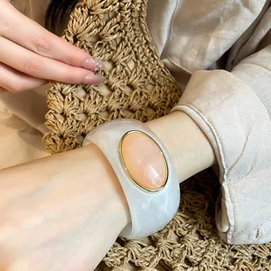 Detailed close-up of a retro oval acrylic wide bangle with elegant marble texture and gold trim