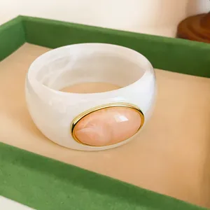 Close-up of a vintage white marbled acrylic wide bangle with a peach oval stone and gold rim