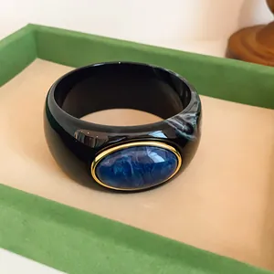 Detailed close-up of a retro black acrylic wide bangle with a blue oval resin stone
