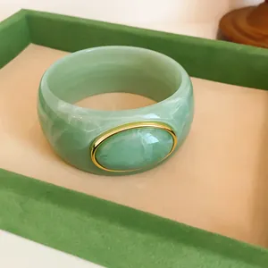 Macro view of the green marble texture and gold-trimmed oval on the acrylic bangle.