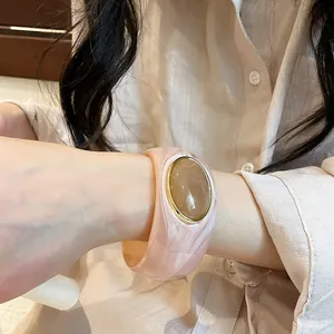 Close-up of retro pink marble acrylic wide bangle with gold-framed oval amber stone