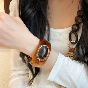 Close-up of a retro amber acrylic wide bangle with an oval faux stone on a woman's wrist