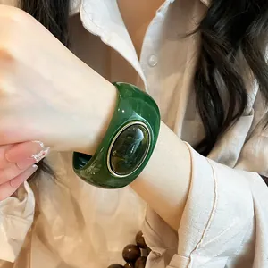 Detail of retro wide green acrylic bangle with oval stone inlay on a woman's wrist.