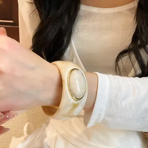 Detail view of a vintage cream marble acrylic wide bangle with an oval gold-rimmed stone