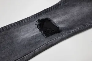 Détail de déchirure usée sur un jean évasé noir délavé vintage pour homme de style high street