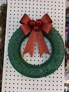 Detail of a green glitter Christmas wreath with a sparkly red bow and baubles.