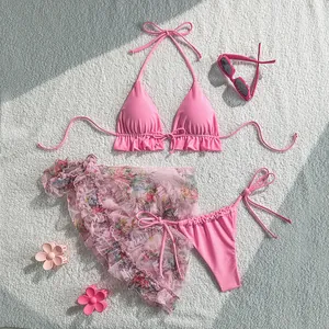 Pink three-piece bikini set with floral mesh sarong and accessories on white rug