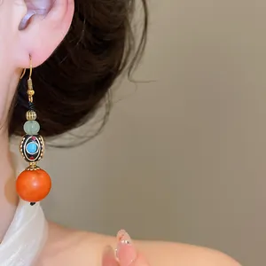 Close-up of ethnic style polymer clay earring with orange bead and intricate design