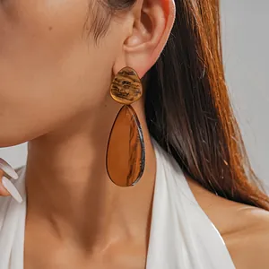 Close-up detail of stylish amber marbled resin water-drop earrings worn by a model