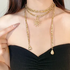 Dettaglio di una collana bohémien dorata a più strati con ciondolo a sole e perline quadrate.