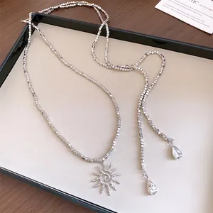 Dettaglio macro di una collana di perle quadrate d'argento con ciondolo sole boho