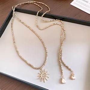 Primo piano della collana lunga boho dorata con ciondolo a sole e perle quadrate geometriche.