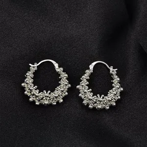 Gros plan de boucles d'oreilles créoles en argent à texture perlée sur soie noire.