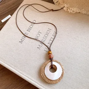 Detailed view of handmade raffia and resin pendant necklace with wooden beads on linen.