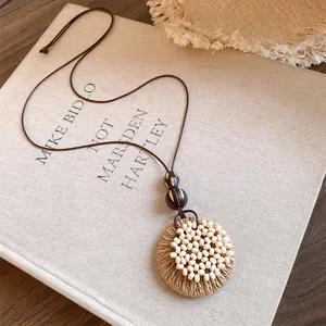 Detailed view of handmade raffia circular pendant necklace on minimalist book cover