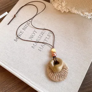 Detailed view of handcrafted raffia and resin pendant necklace on a linen book cover.