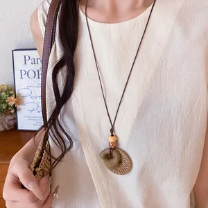 Close-up detail of a boho raffia circular pendant necklace worn with a cream linen top.