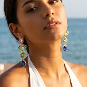 Detail of colorful geometric gemstone drop earrings worn by a model against a sea background