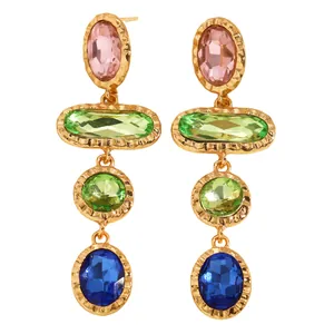 Detailed macro view of geometric gold drop earrings featuring pink, green, and blue crystals