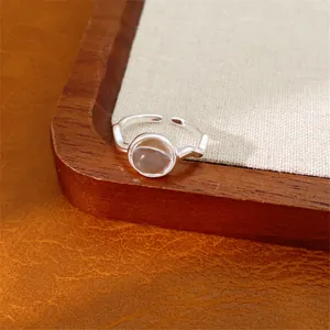 Primo piano di un anello aperto minimalista color argento con pietra di vetro trasparente.