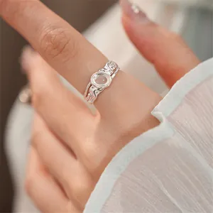 Primo piano di un anello argentato con gemma di vetro ovale e fascia con texture.