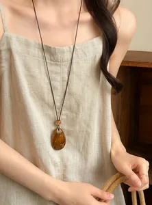 Close-up of retro teardrop amber pendant on a long cord necklace worn by a female model