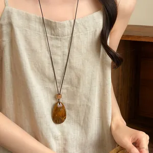 Detail showing a retro amber-colored teardrop swirl pendant on a long dark cord necklace