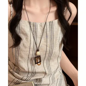 Retro long necklace with geometric pendant on a striped linen dress, elegant detail.